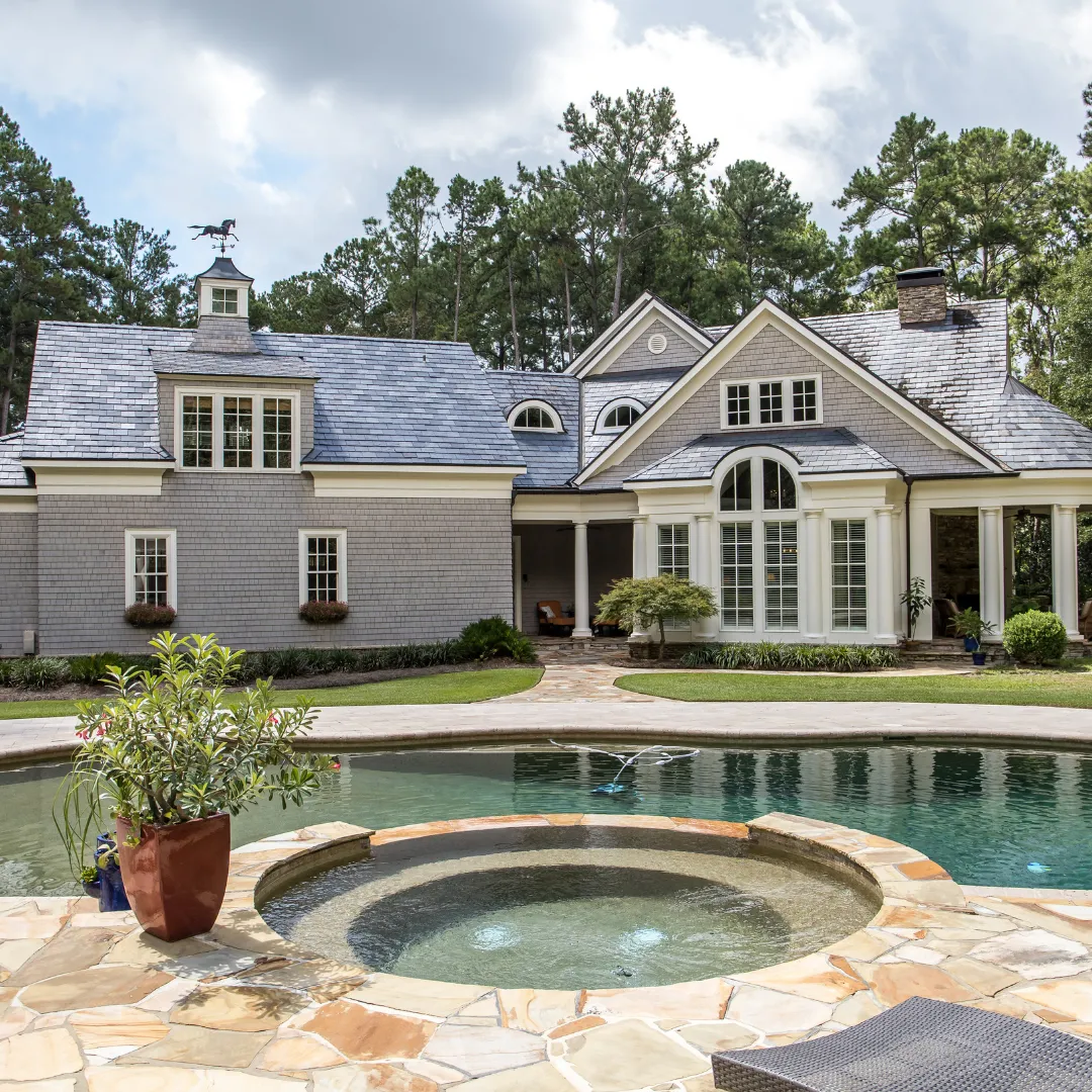 Custom inground swimming pool with an integrated round stone spa, natural stone patio coping, and luxury estate home backdrop in Raleigh, NC.