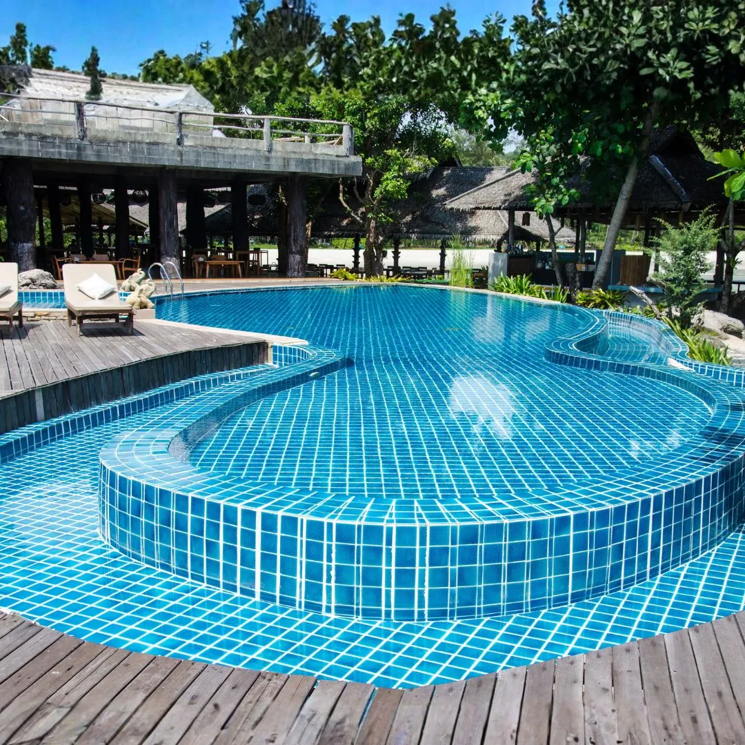 Custom curved inground swimming pool featuring light blue mosaic tiling, raised wood decking, and poolside lounge seating in Raleigh, NC.