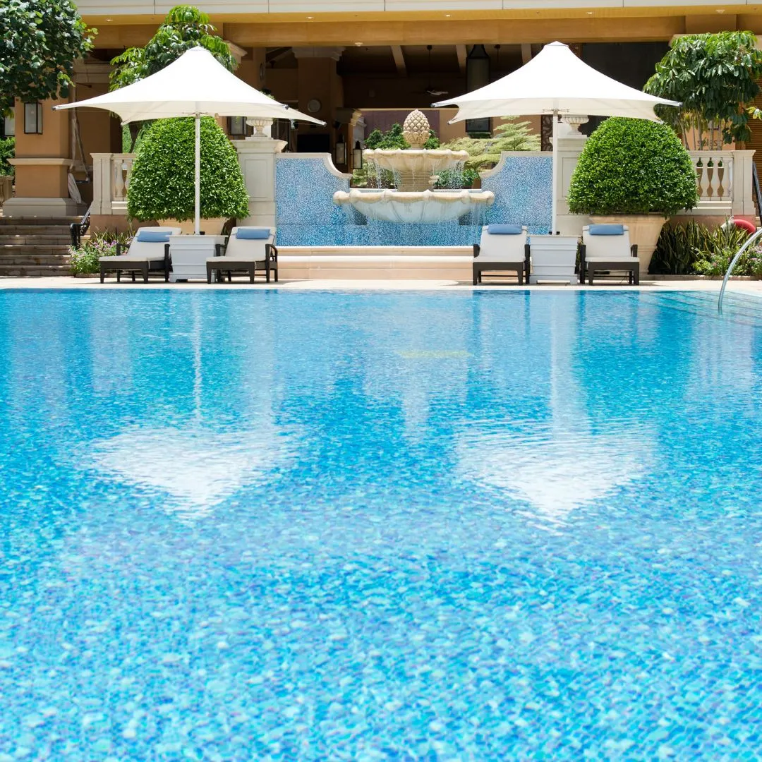 Luxury resort-style inground swimming pool featuring white patio umbrellas, poolside lounge chairs, and stone fountain spillways in Raleigh, NC.