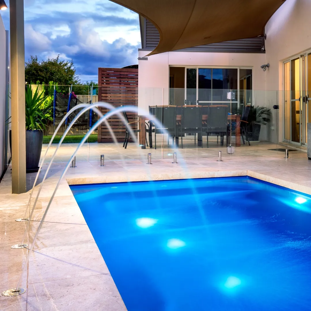 Illuminated custom inground pool with deck water jets, blue underwater LED lighting, and stone paver patio in Raleigh, NC.