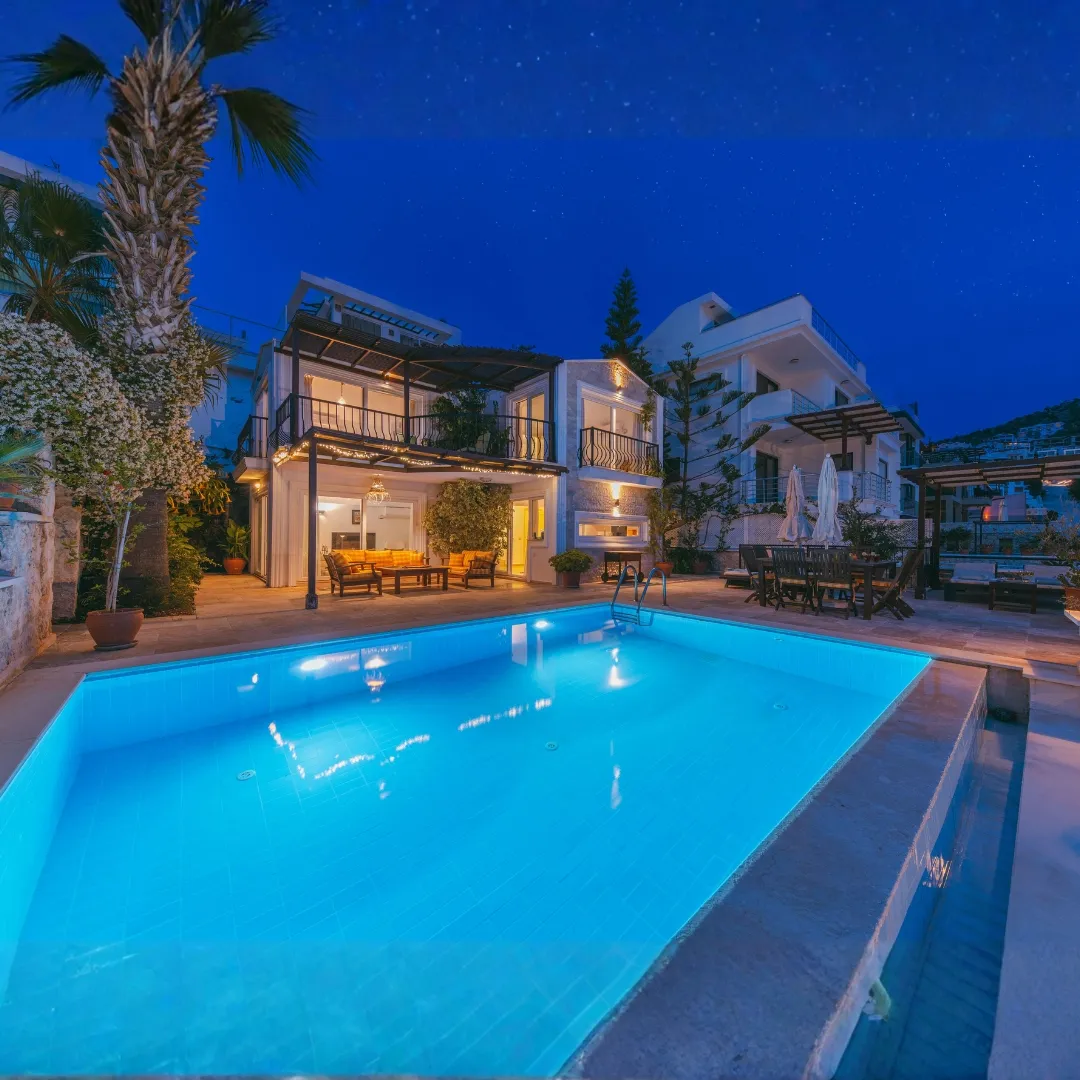 Illuminated luxury inground swimming pool with blue underwater lighting and stone patio at dusk behind a two-story home in Raleigh, NC.