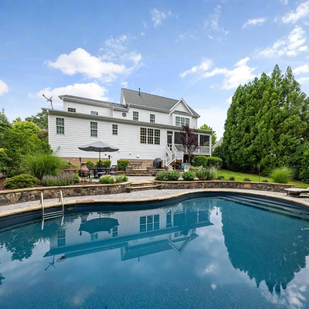 Custom curved inground swimming pool with deep blue water behind a two-story home, featuring elevated deck stairs and manicured backyard landscaping in Raleigh, NC.