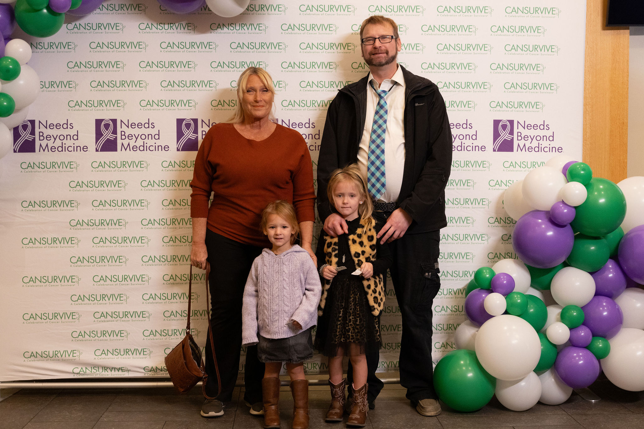 Two adults and two children standing in front of a CANSURVIVE and Needs Beyond Medicine backdrop.