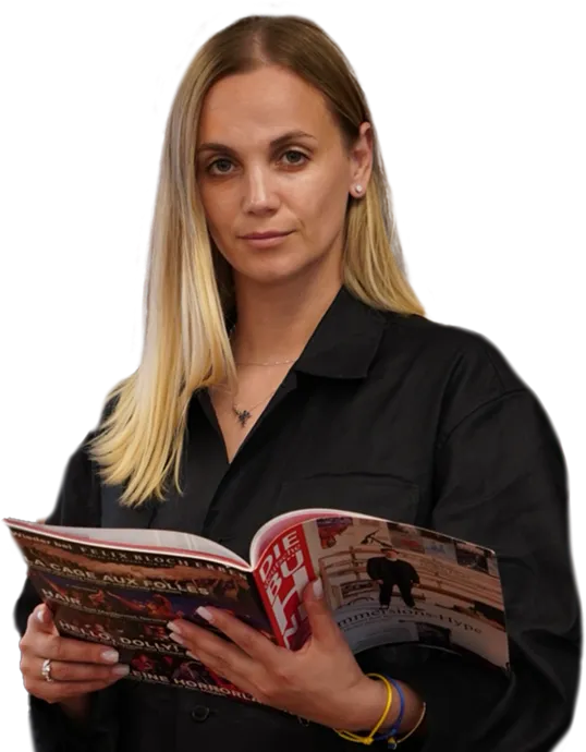 Woman with long blonde hair wearing a black shirt, holding and reading a magazine.