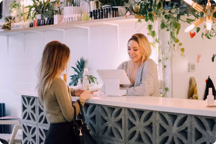 Woman customer interacting with smiling store cashier at a plant-adorned counter.