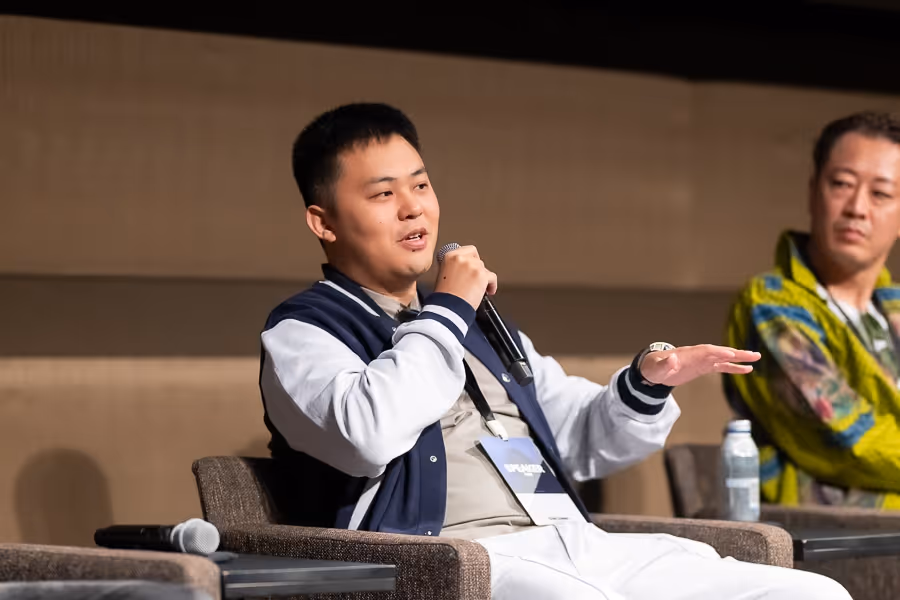 マイクを持ち、話している紺色のジャケットを着た男性。