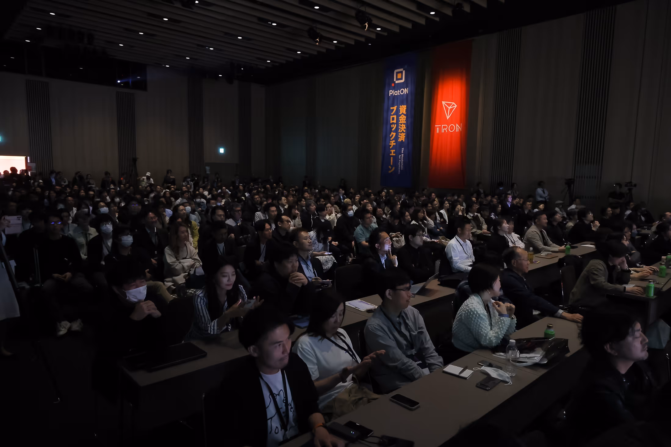 会議室で前方に向かって講演を聞いている多くの聴衆。