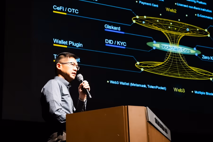 マイクを持ち、テクノロジー関連の図を背景にしたプレゼンテーションを行う男性。