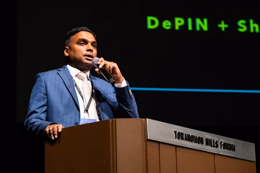 スーツ姿の男性がTORANOMON HILLS FORUMの壇上でマイクを持って話している。