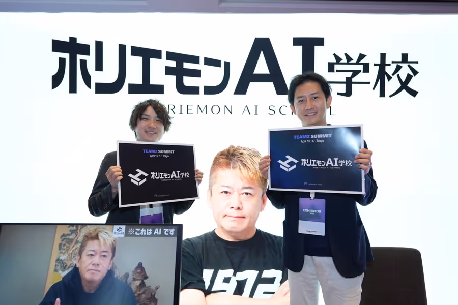 ホリエモンAI学校の前で2人の男性が看板を持ち、中央の大きなスクリーンに別の男性の顔が映っている。
