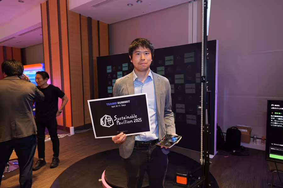 男性がSustainable Pavilion 2025と書かれたサインを手に持っている会議室の中の写真。