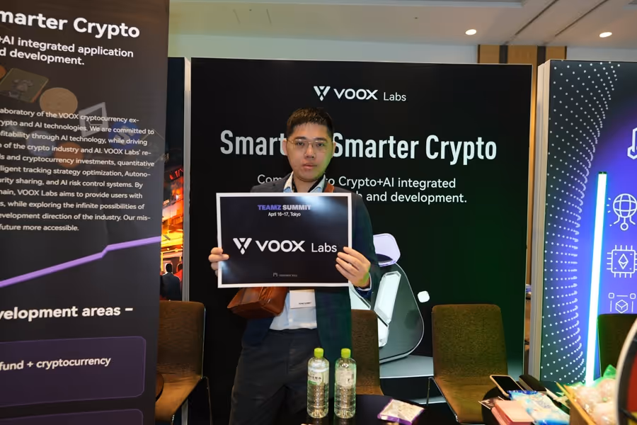 スーツを着た男性がオフィス展示会で『VOOX Labs』と書かれた看板を持っている。