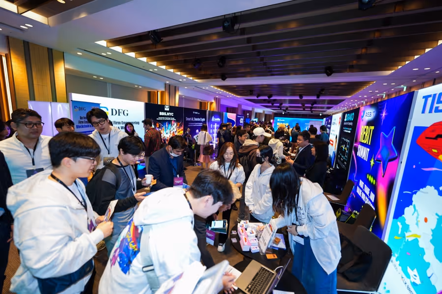 多くの参加者が展示ブースで交流し、壁にカラフルな広告パネルが並ぶ賑やかな会議室の展示会風景。