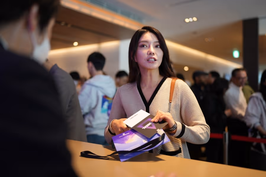 受付カウンターで複数のチケットやパンフレットを手に持ち、話している女性。