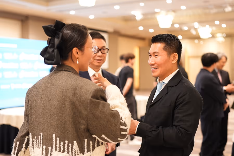 フォーマルな服装で会話する男女が明るい会場にいる。