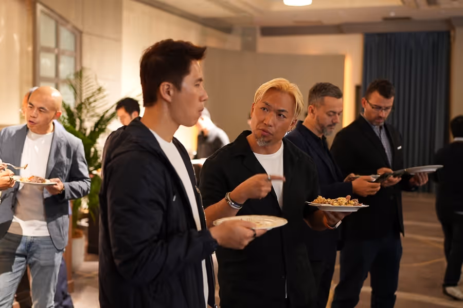 食事を持ち、室内で会話やスマホを操作している5人の男性たち。