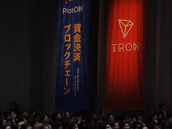 多くの聴衆がいる部屋の壁に掛けられた青いPlatONの資金決済ブロックチェーンの垂れ幕と赤いTRONの垂れ幕。