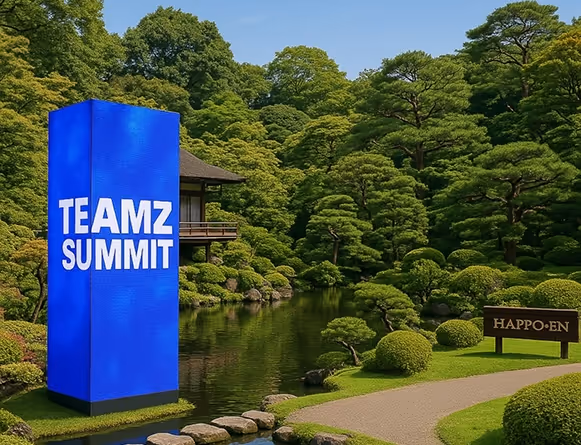 富士山庭園の池のそばに、青い背景に白い文字で「TEAMZ SUMMIT」と表示された巨大なLED塔。