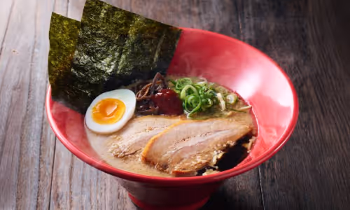 豚骨スープにチャーシュー、半熟卵、のり、ネギ、きくらげをのせた赤い器のラーメン。