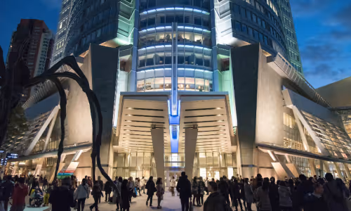 夜の都市広場に集まる人々と、近代的な高層ビルの明るく照らされた入り口。