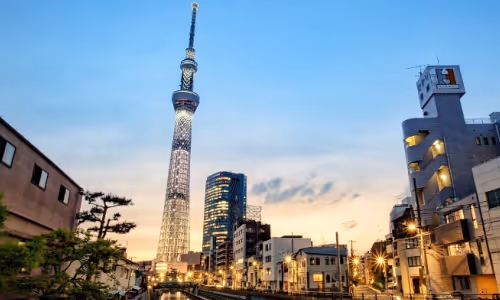 夕暮れ時にライトアップされた東京スカイツリーと周囲の都市の高層ビル。