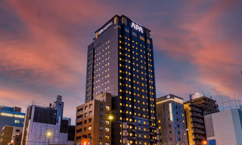 夕暮れ時の空を背景にライトが灯ったAPAホテルの高層ビル。