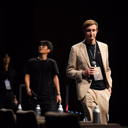 スーツを着た男性がマイクを持ち、舞台でVIPバッジを提示している。