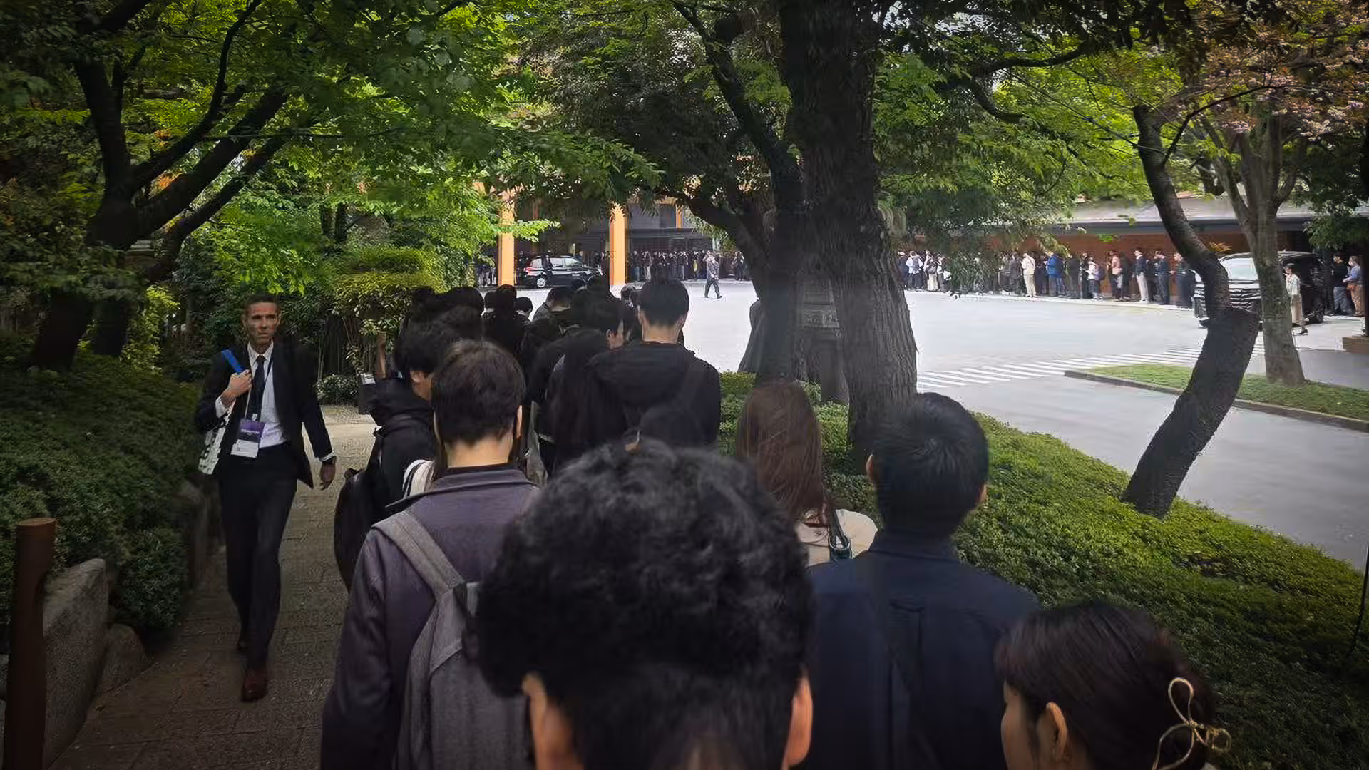 緑豊かな歩道に沿って並ぶ多くの人々の列。