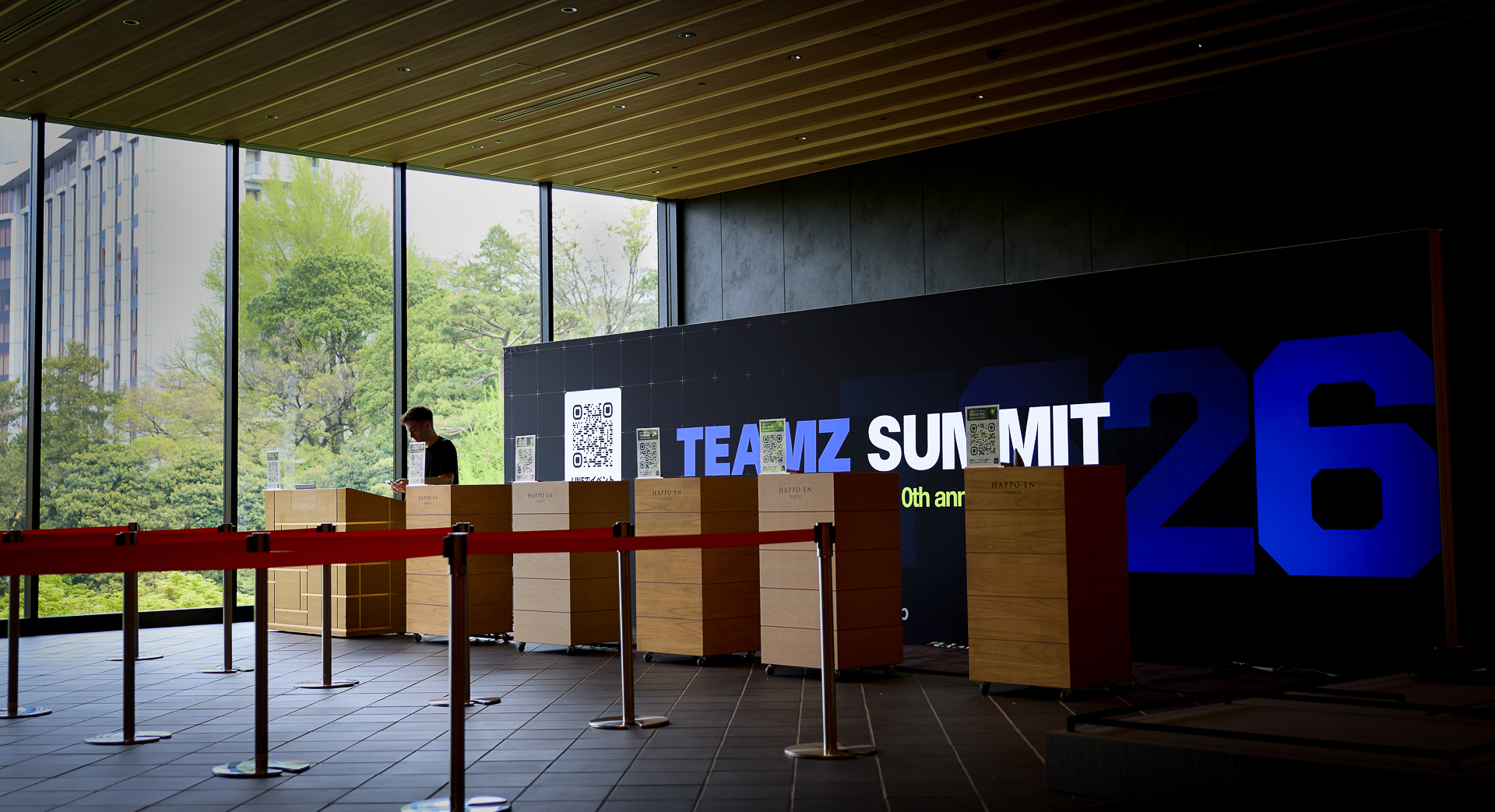 会場の受付カウンターが並び、背景に「TEAMZ SUMMIT 26」の文字が大きく表示されているホールの内観。