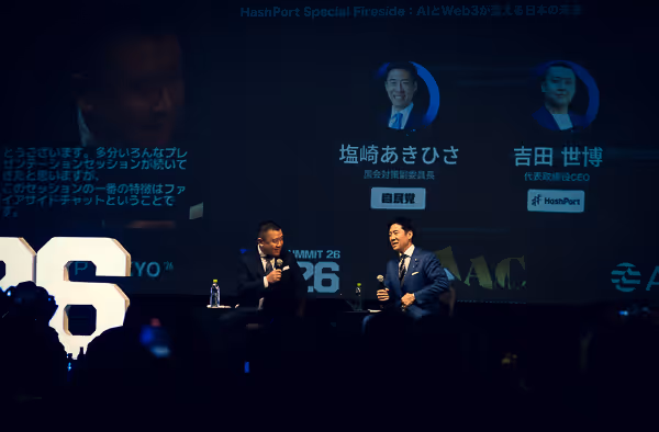 舞台上で対談する二人の男性、背景に塩崎あきひさと吉田世博の顔写真と名前が映し出されている。