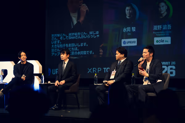 4人の男性が舞台で座り、1人がマイクを持って話しているパネルディスカッションの様子。
