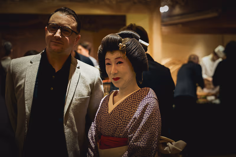 着物を着た女性とメガネをかけた男性がパーティーで並んで立っている。