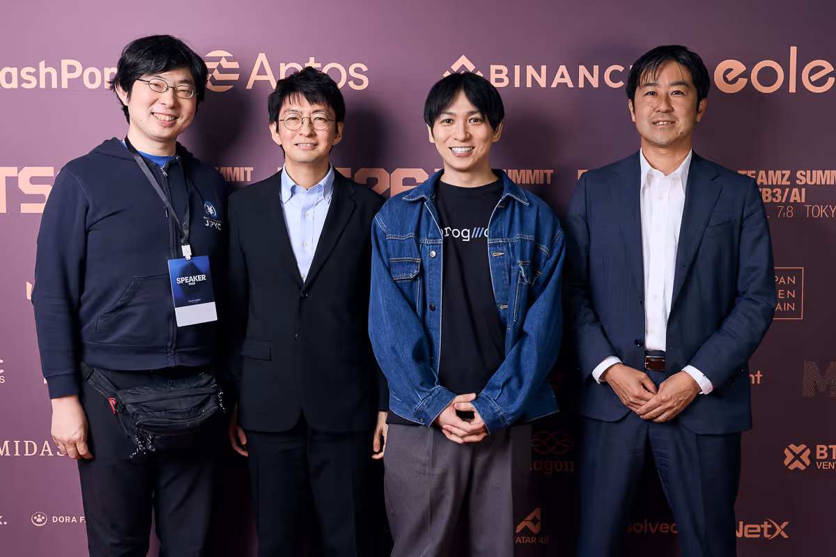 4人の男性が業界イベントの背景の前で笑顔で立っている。