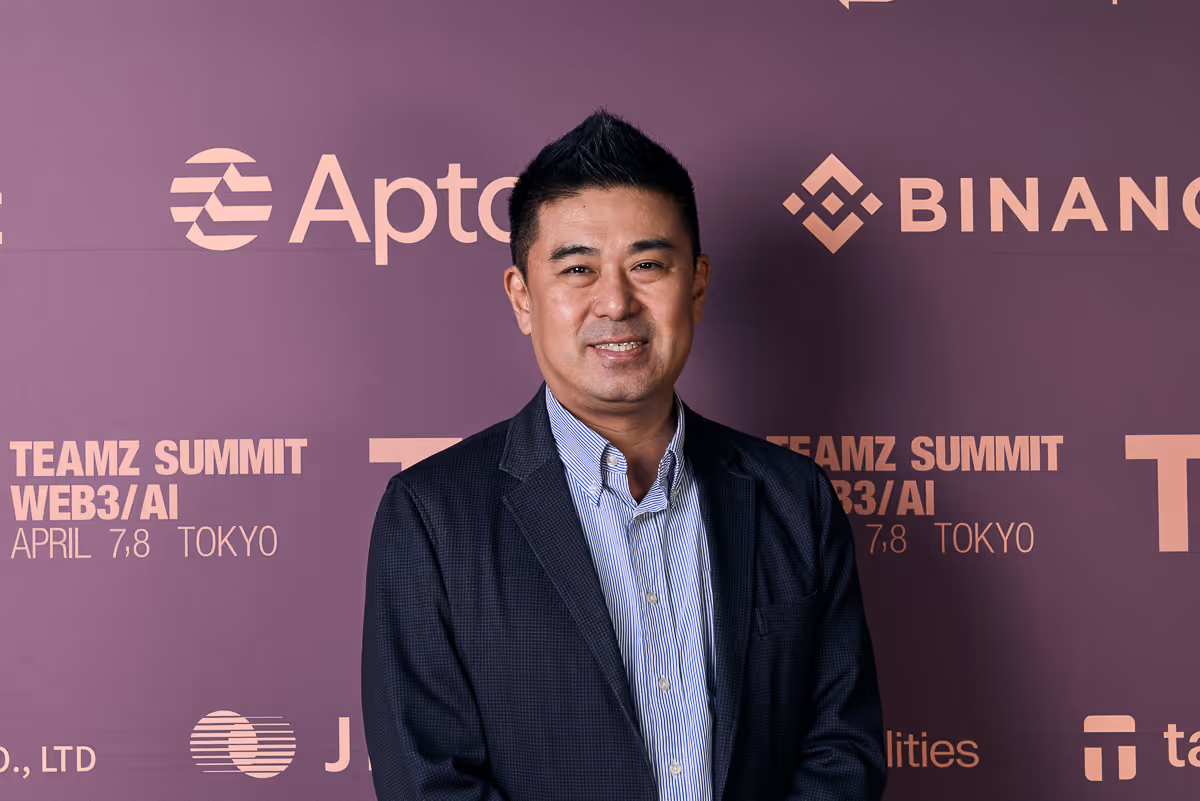 東京でのTEAMZ SUMMIT WEB3/AIイベントでネイビーのジャケットとブルーのストライプシャツを着た笑顔の男性。