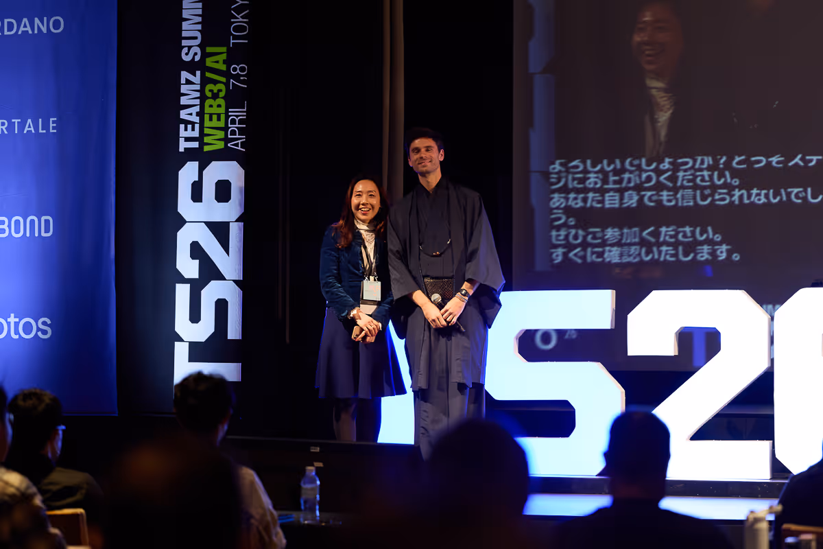 ステージ上に立つ2人のスピーカーと観客席のシルエット、背後に大きな白い数字「526」とイベントのバナー。