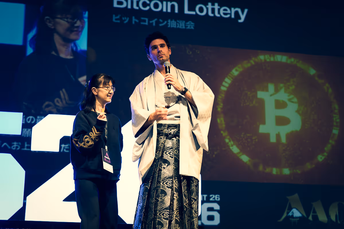 マイクを持ち、伝統的な和服を着た男性と黒いスウェットを着た女性がビットコイン抽選会のステージに立っている。