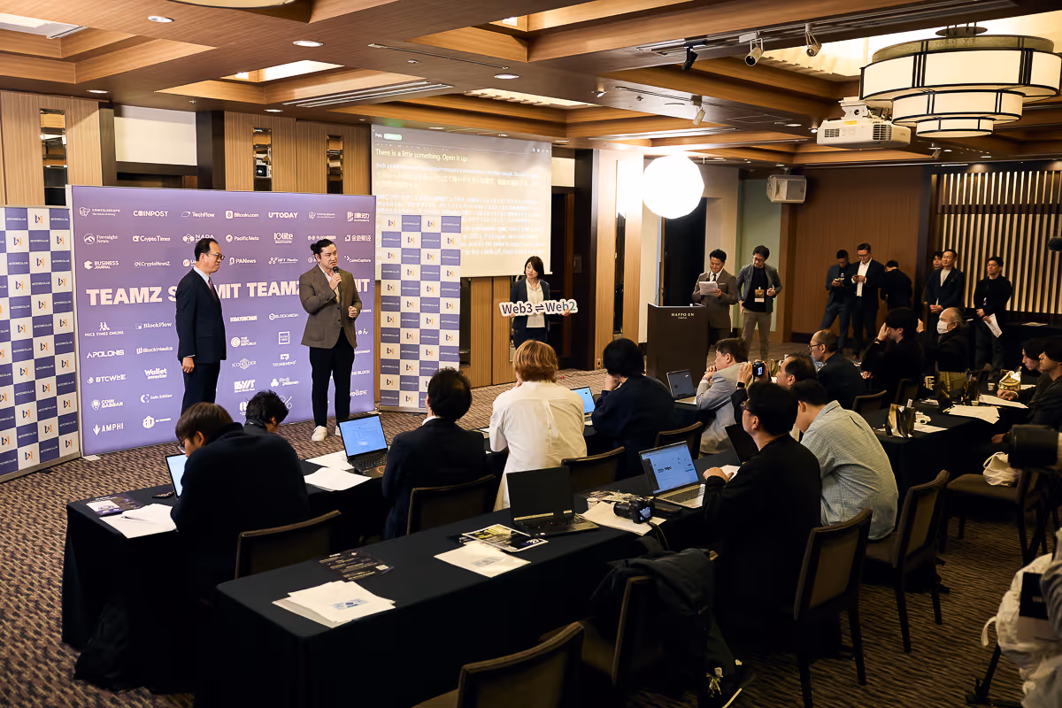 会議室で発表を行う2人のスピーカーと、参加者がノートパソコンでメモを取るビジネスイベントの様子。