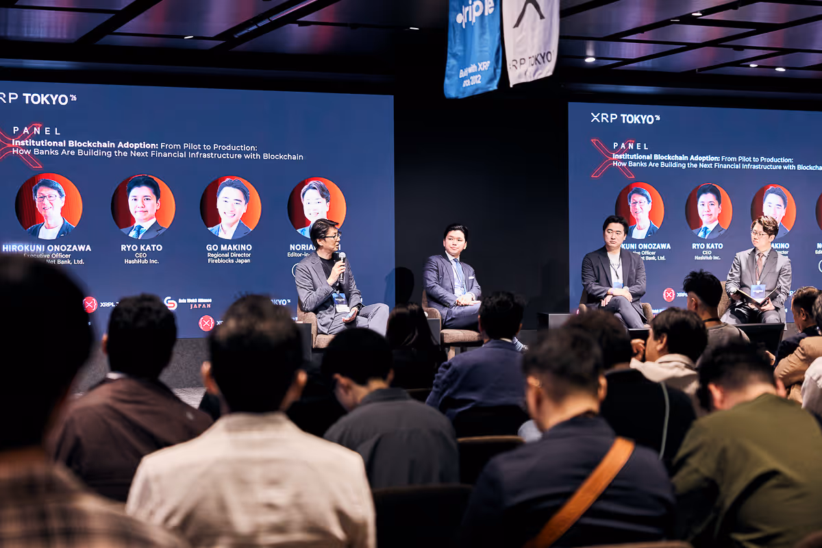 暗い会場で、XRP TOKYOのパネルディスカッションが行われ、多くの観客が着席している。