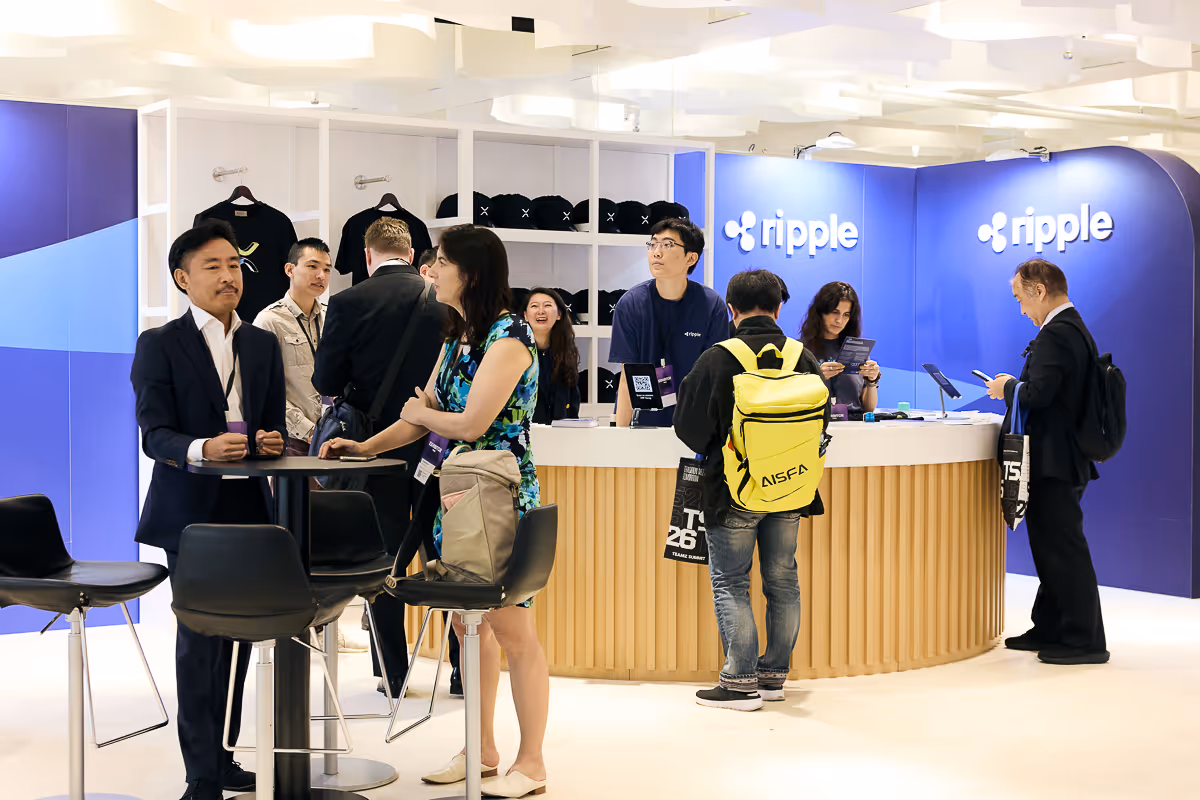 リップルのブースでビジネスカジュアルな服装の複数の人々が交流している会場。