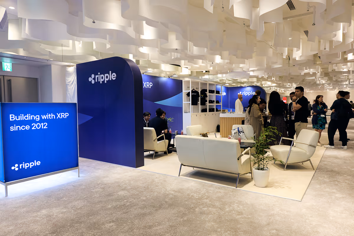 Rippleのブースで「Building with XRP since 2012」と表示された青い看板と、ソファ席で話す人々。