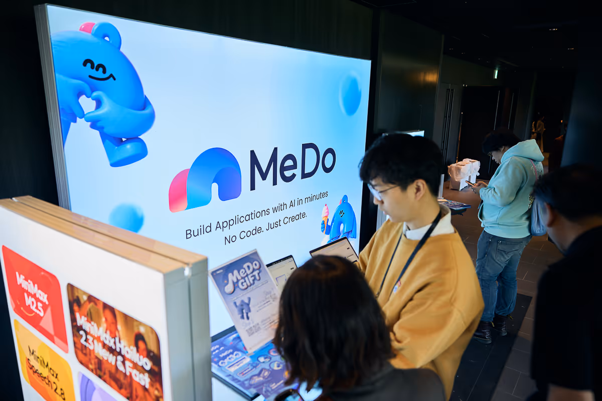 人々がスマートフォンを使い、MeDoのAIアプリケーション開発サービスの展示の前に立っている。