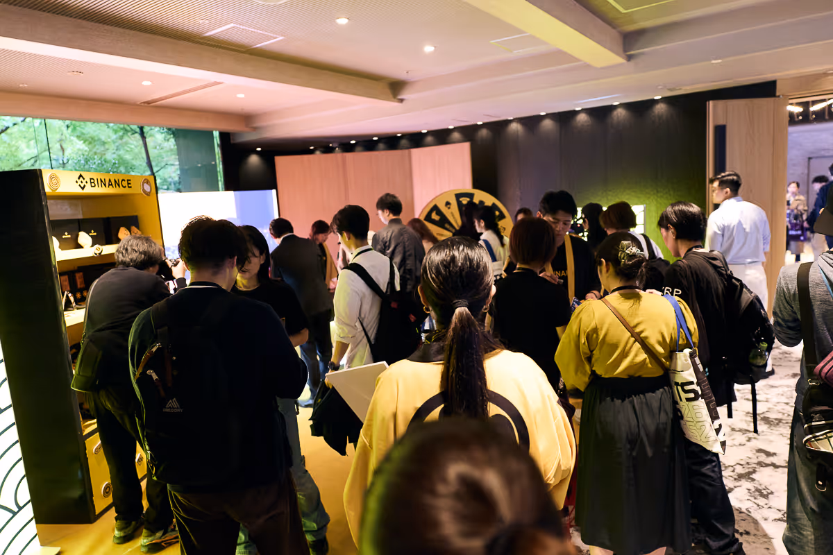 バイナンスのブースで交流や展示を楽しむ多くの人々が集まっている室内イベントの様子。