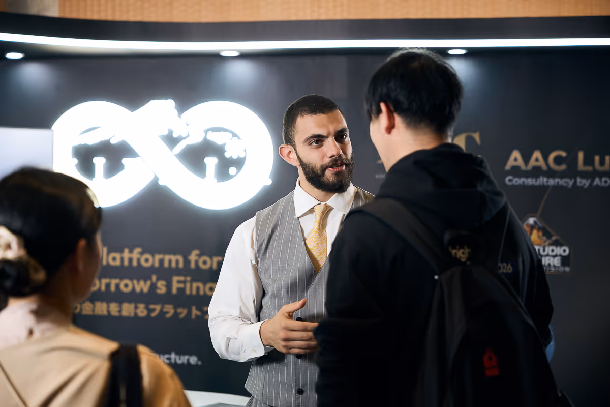ギターを持った男性が黒いフード付きジャケットを着た男性と話している展示会のブース。