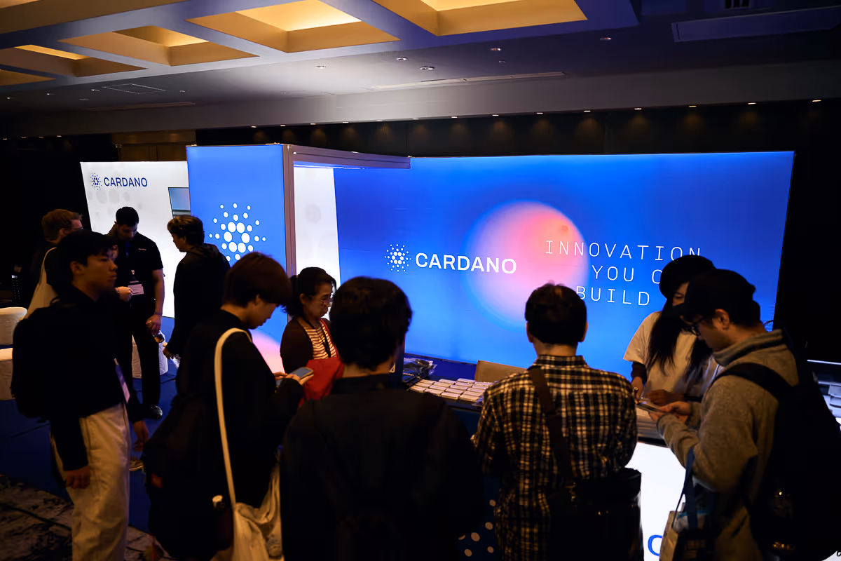 複数の人々が集まるCardanoの展示ブース、背景に『INNOVATION YOU CAN BUILD』の文字。