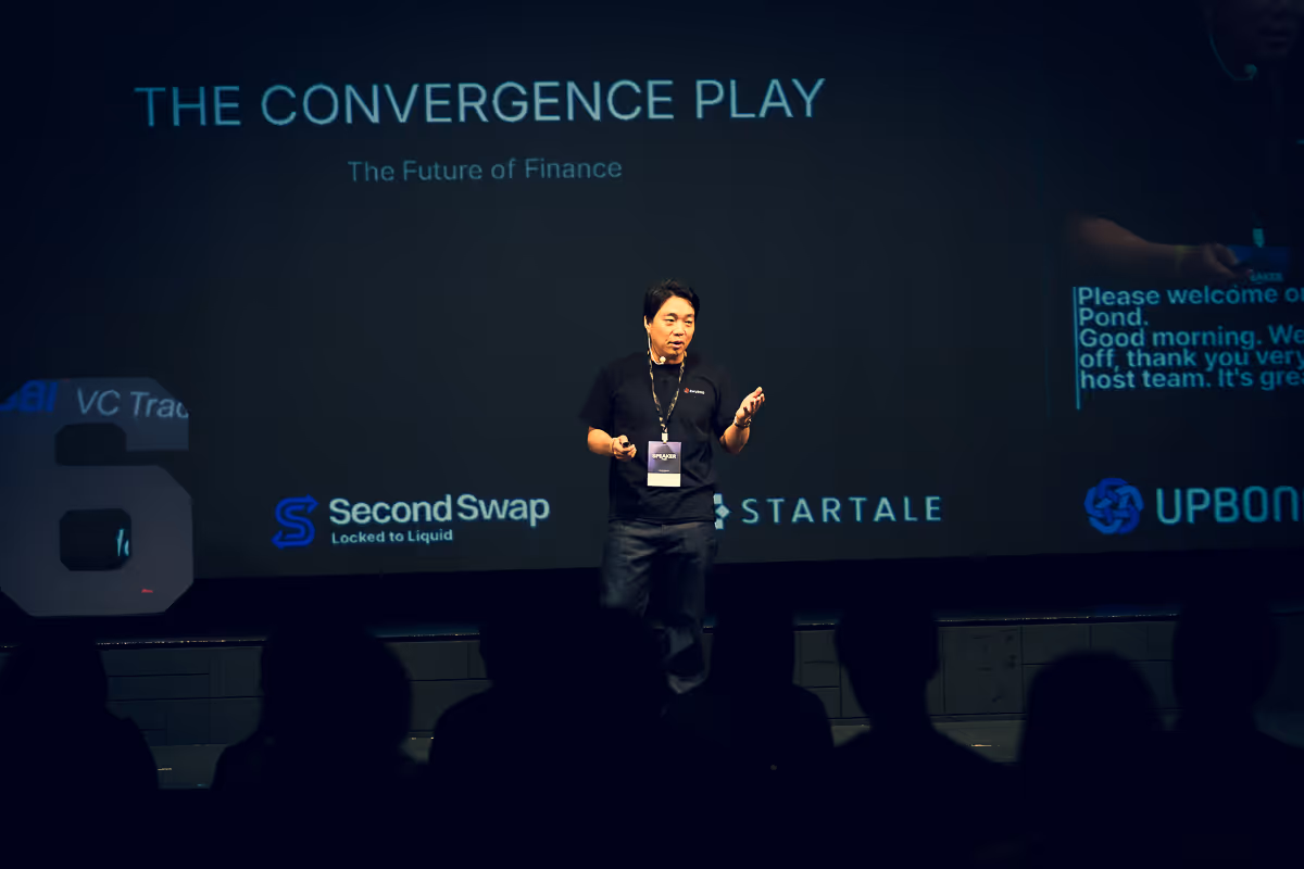 男性スピーカーが「THE CONVERGENCE PLAY The Future of Finance」のスライド前でプレゼンテーションを行っている。