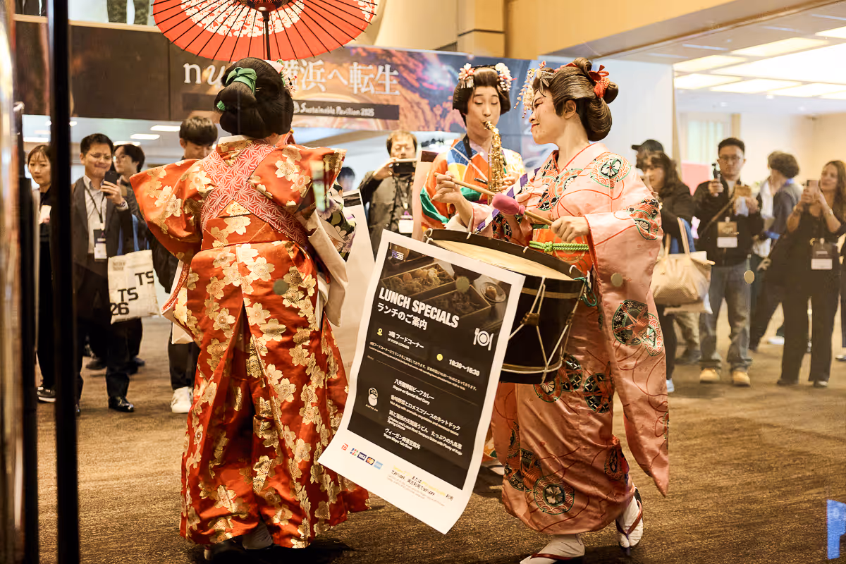 伝統的な着物を着た女性たちが屋内で太鼓やサックスを演奏しながら踊っている様子。