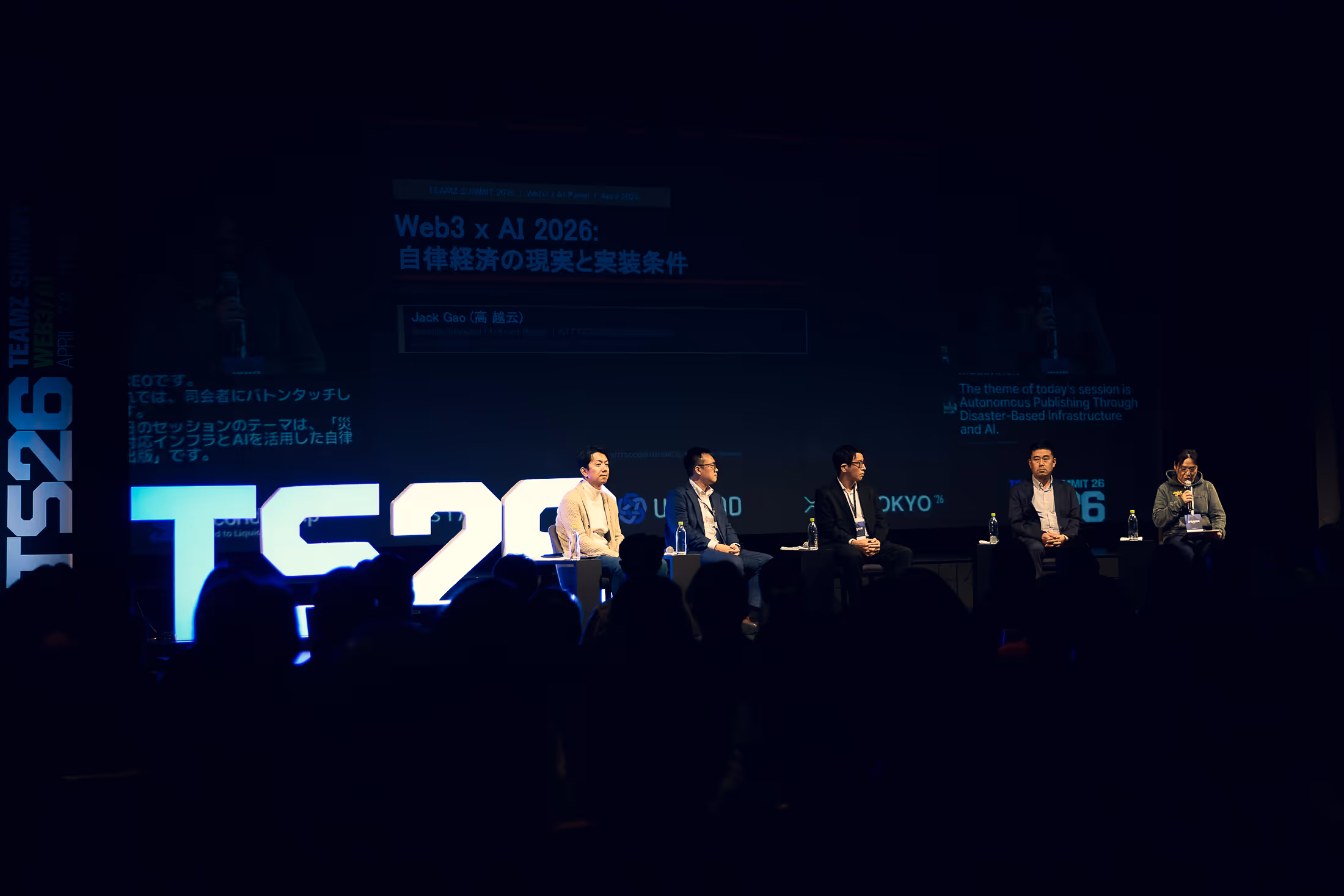 Web3 x AI 2026のパネルディスカッションでステージに座る5人のパネリストと暗闇の中の聴衆。