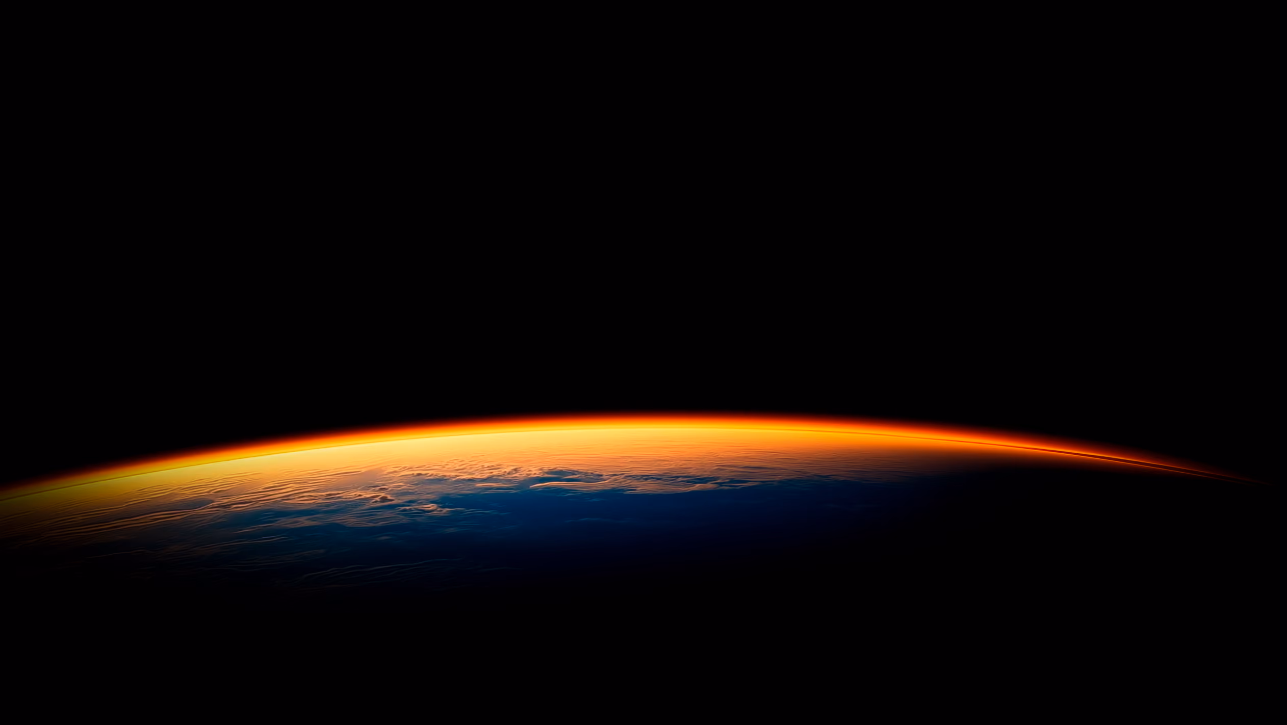 地平線から昇るオレンジ色の太陽の光で照らされ、青と黒のグラデーションが広がる地球の一部。
