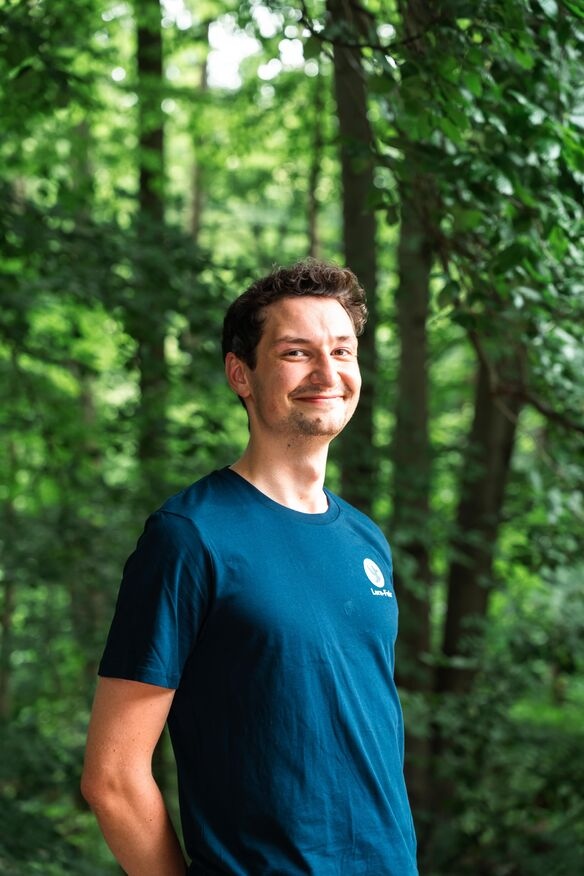 Junge Frau in Lern-Fair T-Shirt vor Wald mit Eulen Maskottchen