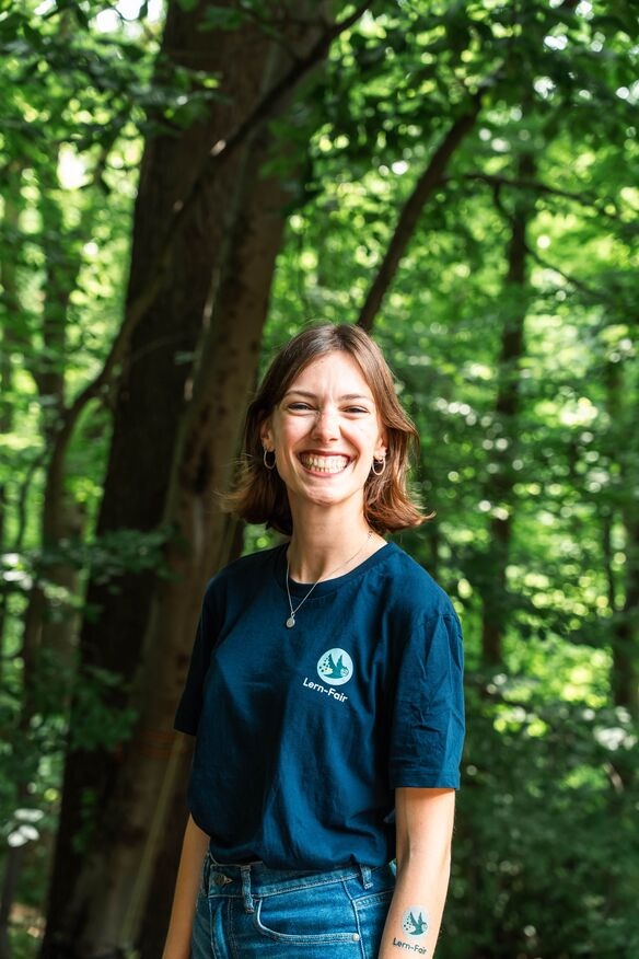 Junge Frau in Lern-Fair T-Shirt vor Wald 
